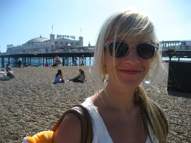 In the image there is a woman in blond hair standing on beach and behind there are many people...