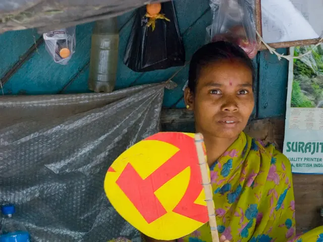 In this image there is a woman sitting on the floor by holding the floor by holding the hand fan....