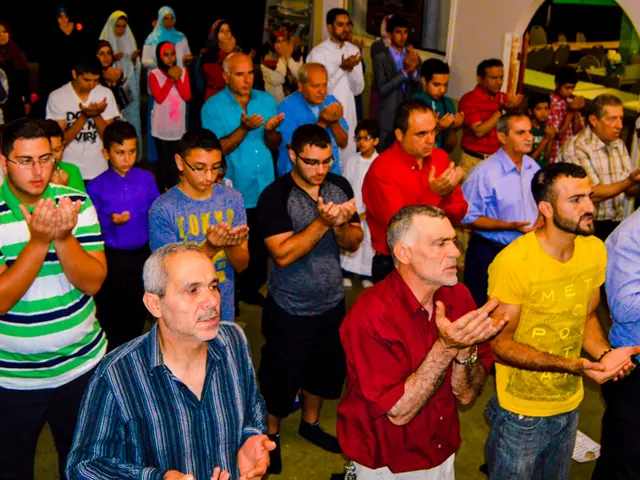 In this image people are praying in a hall, in the bottom left there is some text.